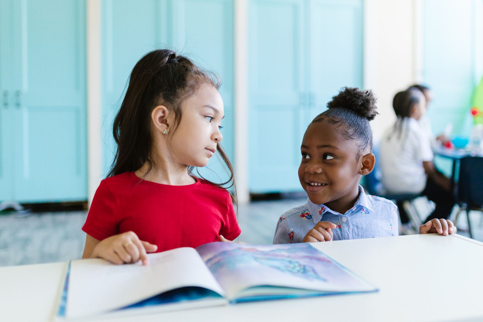 Two girls sharing a picture book in a classroom